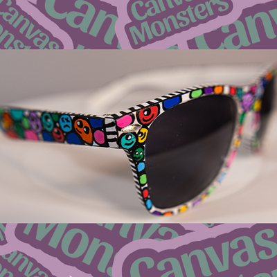A pair of painted sunglasses with colorful character patterns on the frame, displayed on a white background with 'Canvas Monsters' text.