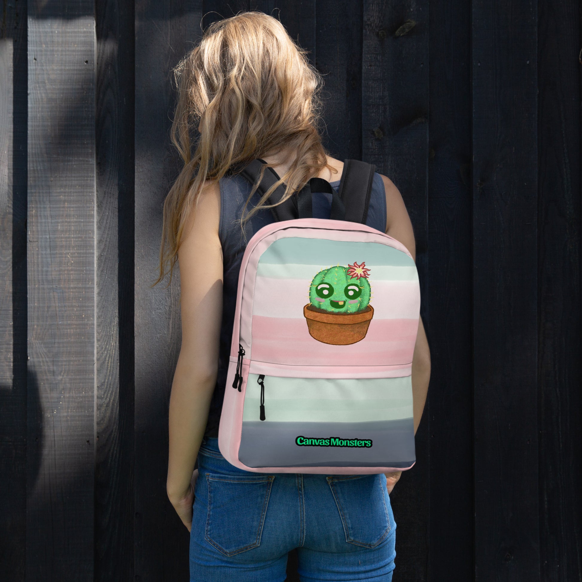 A woman viewed from behind wearing a pastel striped backpack with a cute cartoon cactus in a pot. The backpack features pink, light blue, and gray horizontal stripes, a gray bottom panel with a green 'Canvas Monsters' logo, and a front zippered pocket.