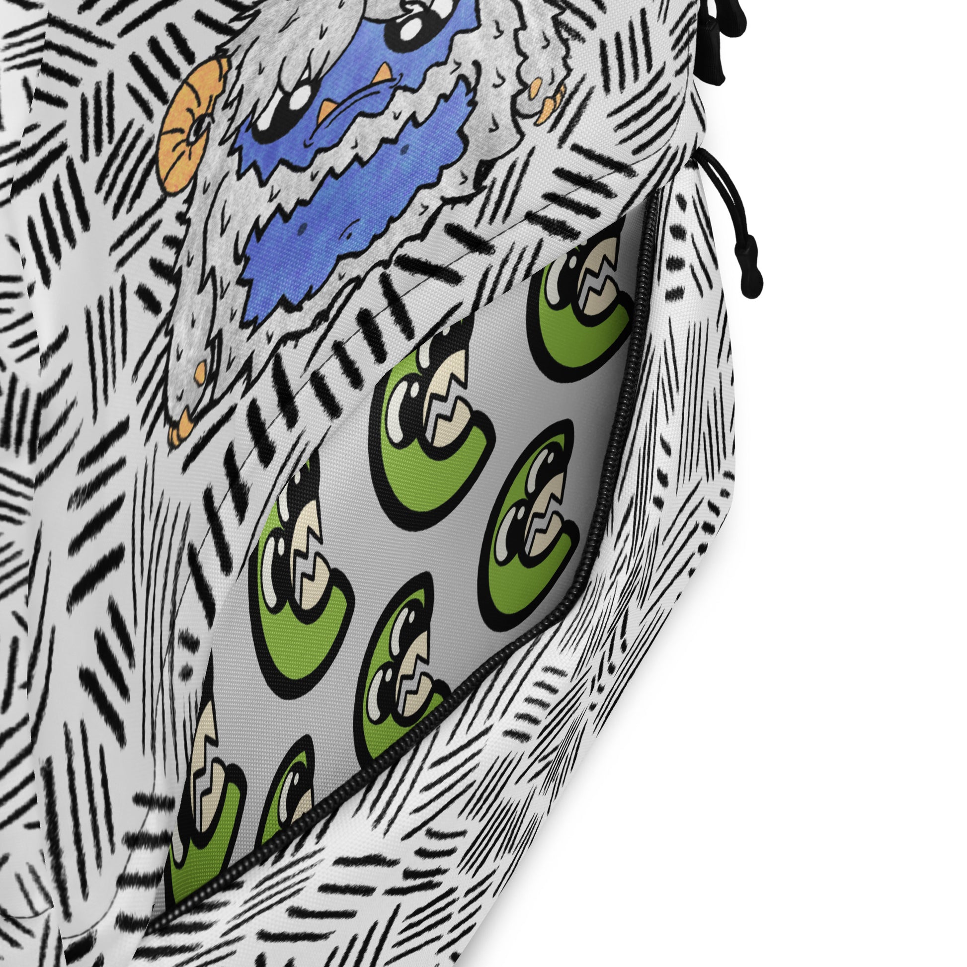 Close-up of a patterned zippered pouch or bag, showing a black-and-white hand-drawn sketch style exterior with a blue and orange cartoon face, and a gray interior lined with green cartoon eyes.