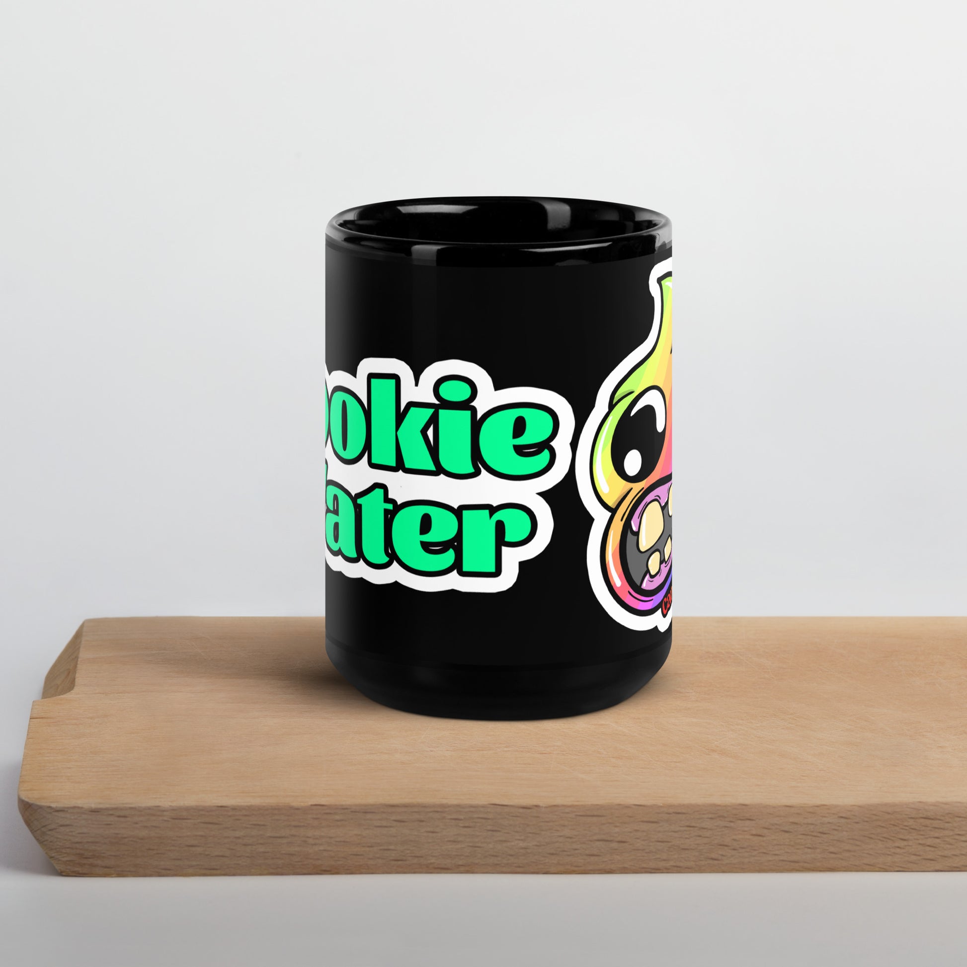 Black mug with 'Dookie Water' text and rainbow poop cartoon character, sitting on a wooden block with a white background.