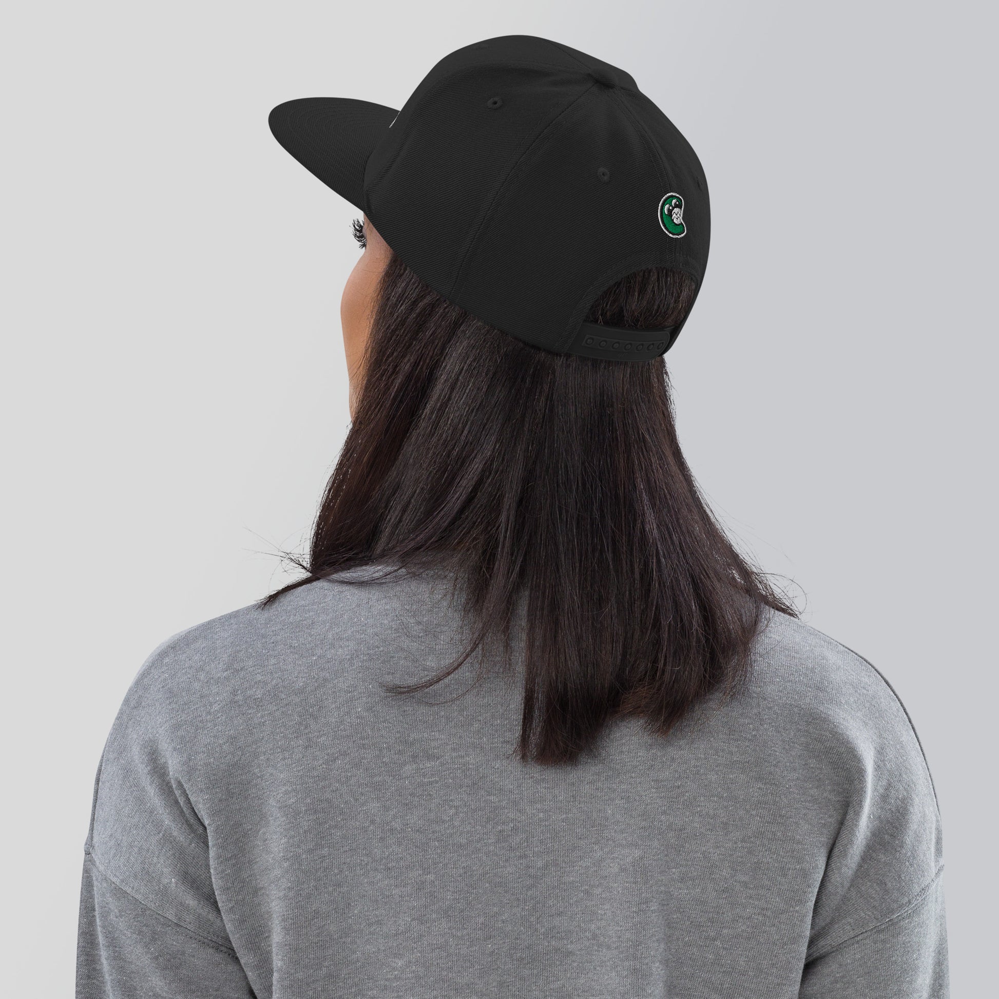 Person wearing a black cap with a logo on the back against a plain background