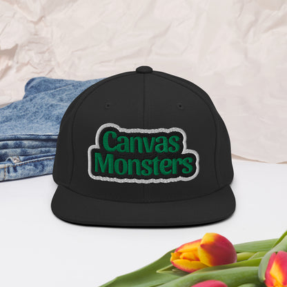 Black cap with 'Canvas Monsters' logo on a white surface with tulips and denim jeans.