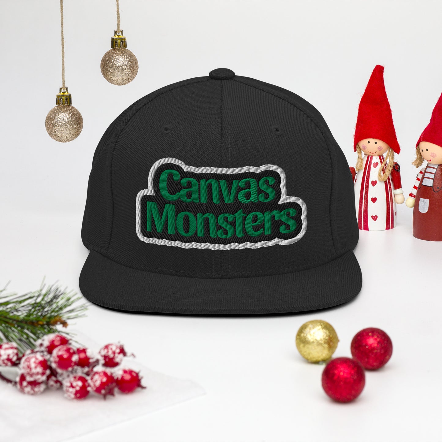 Black cap with 'Canvas Monsters' text on a white background with Christmas decorations.
