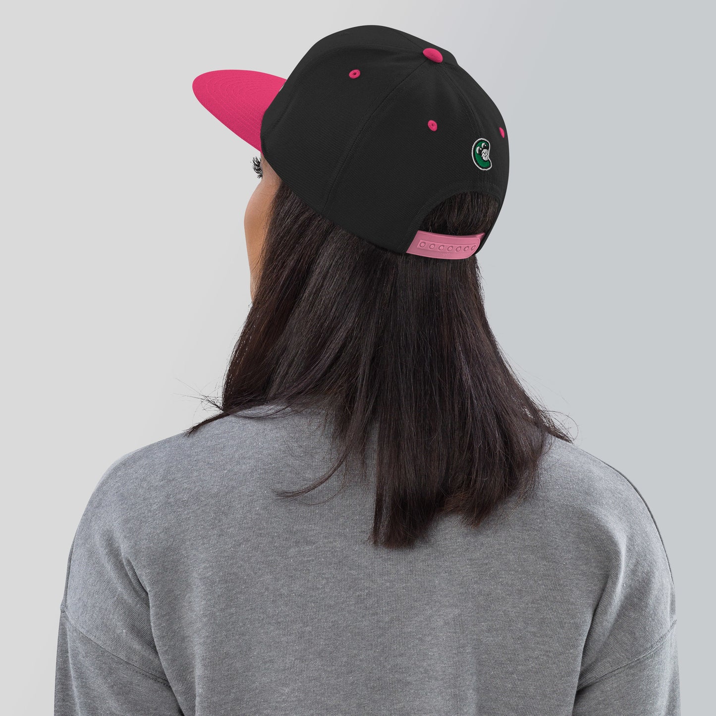 Person wearing a black and pink cap with a logo on a plain background