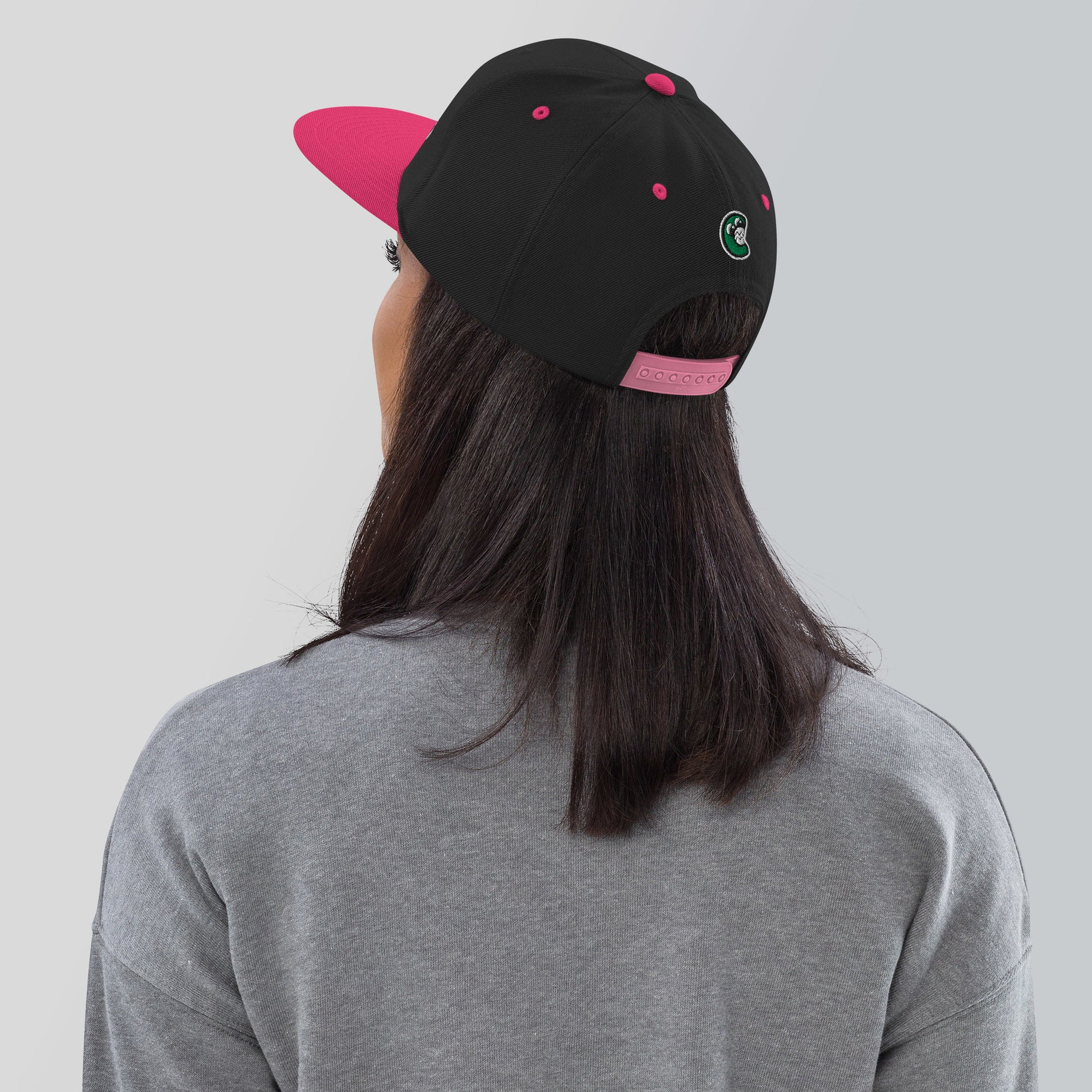 Person wearing a black and pink cap with a logo on a plain background