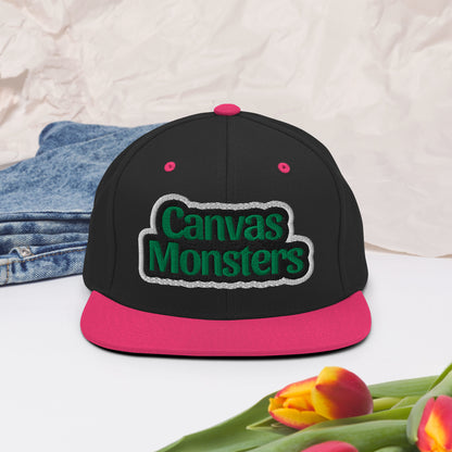 Black and pink cap with 'Canvas Monsters' logo on a light background with denim and tulips.