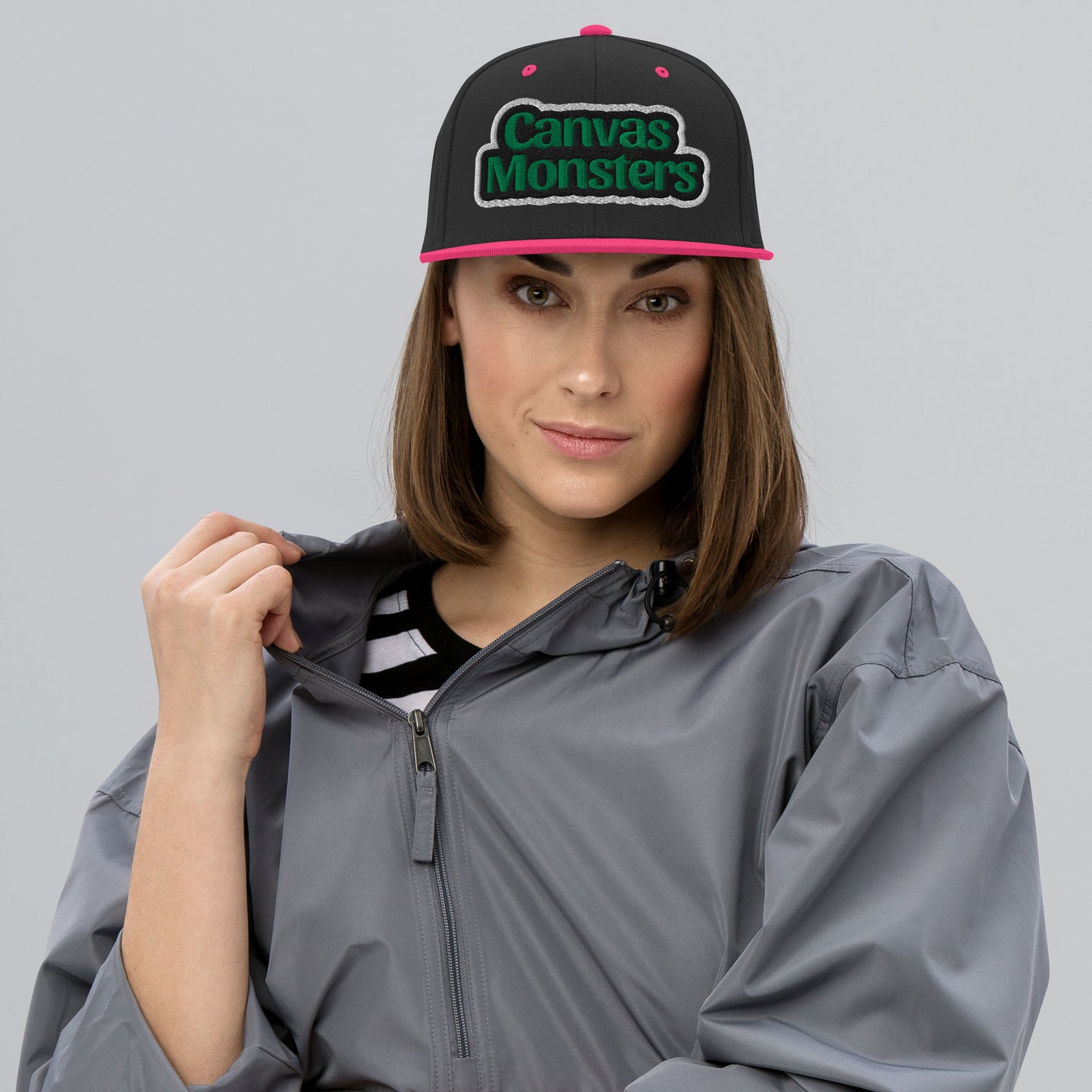 Person wearing a gray raincoat and a black cap with 'Canvas Monsters' logo on a gray background