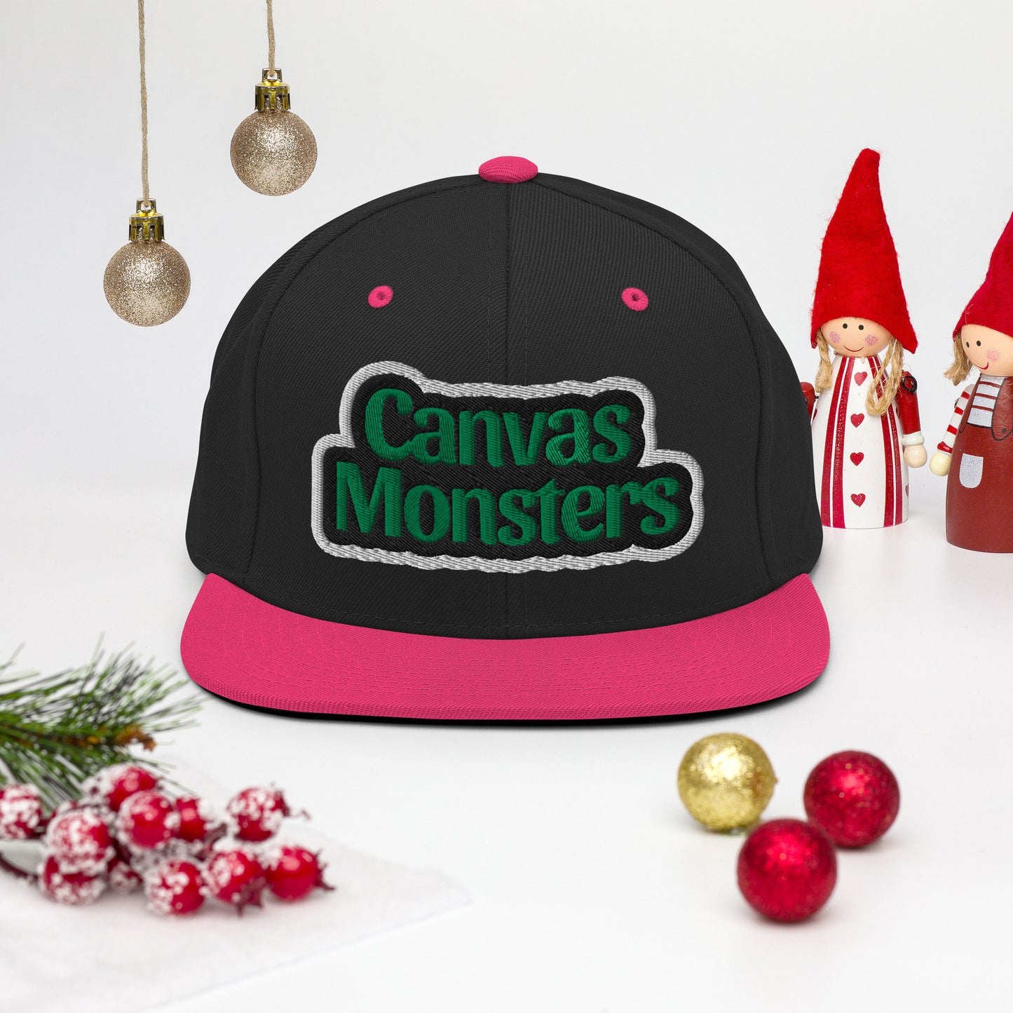 Black and pink cap with 'Canvas Monsters' text, surrounded by Christmas decorations on a white background