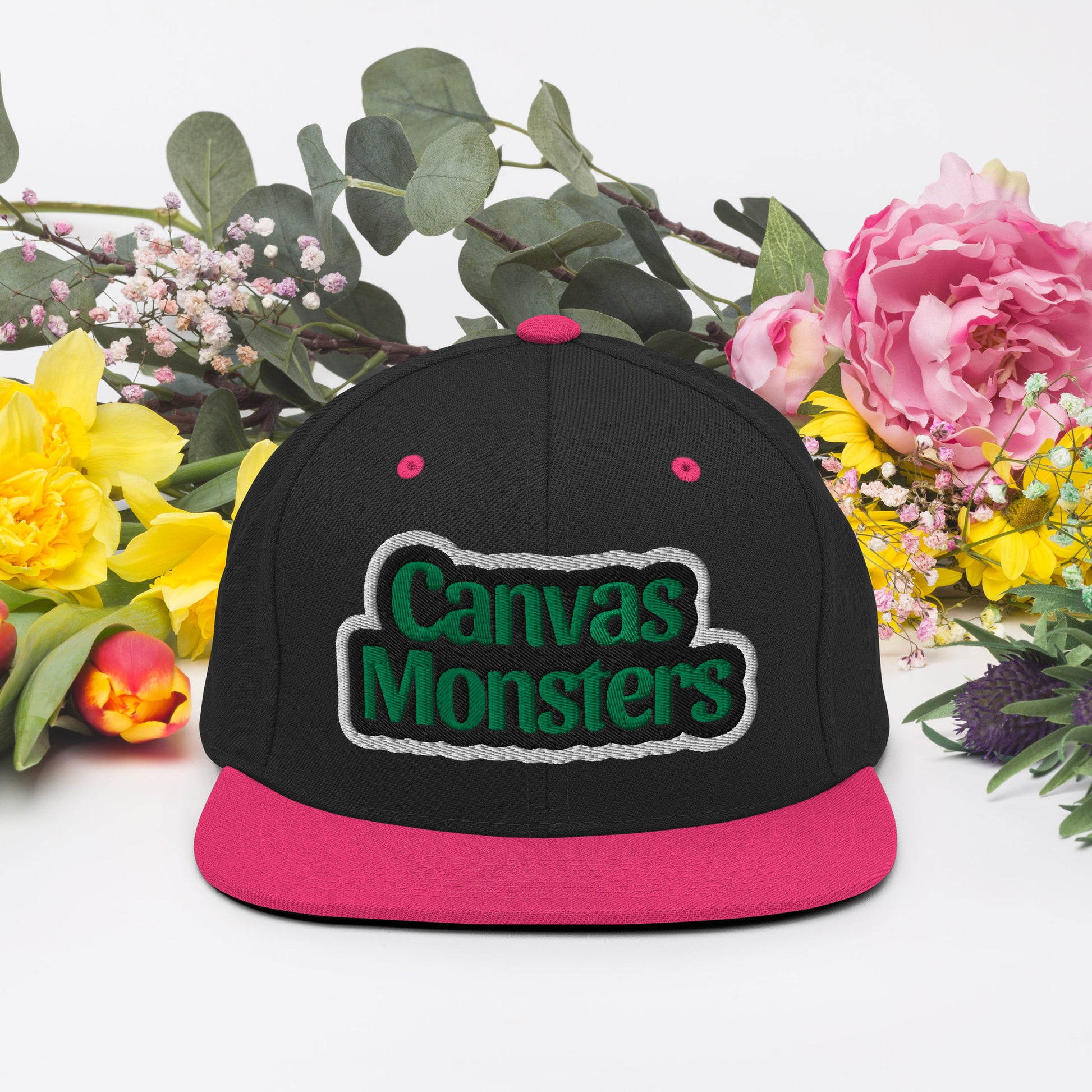 Black and pink cap with 'Canvas Monsters' text, surrounded by flowers on a white background