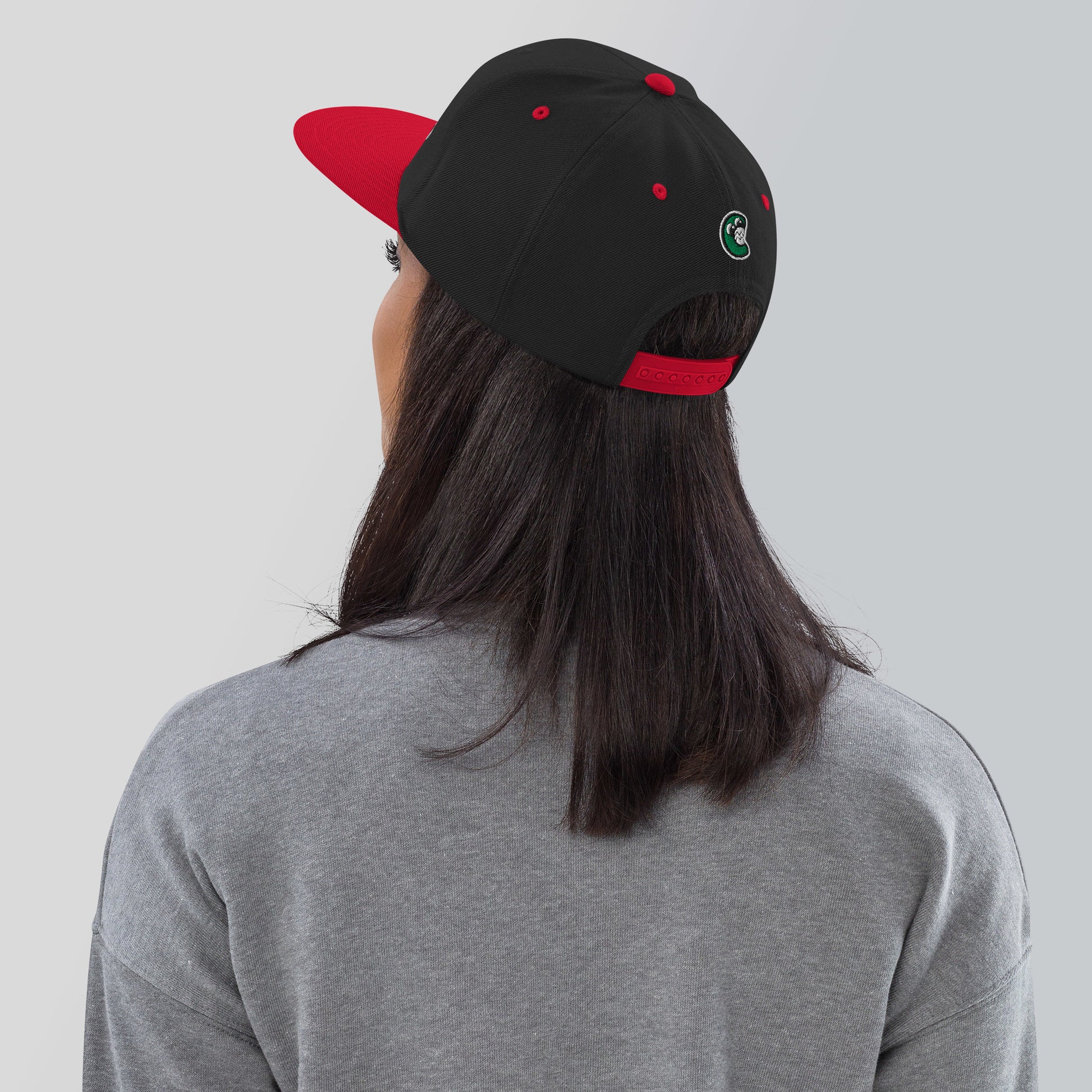 Person wearing a black and red cap with a logo on a plain background