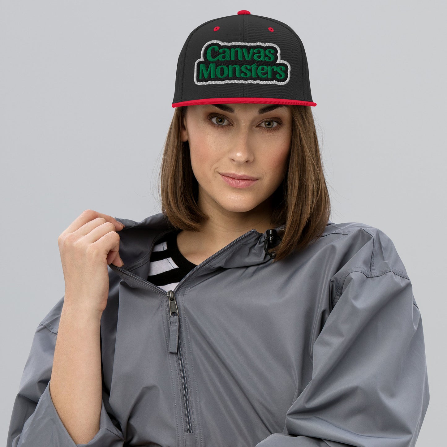Person wearing a gray raincoat and a black cap with 'Canvas Monsters' logo on a gray background
