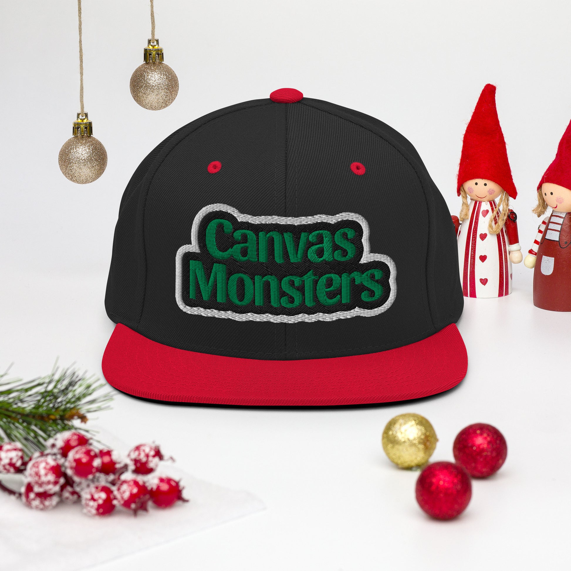 Black and red cap with 'Canvas Monsters' logo on a white background with Christmas decorations.