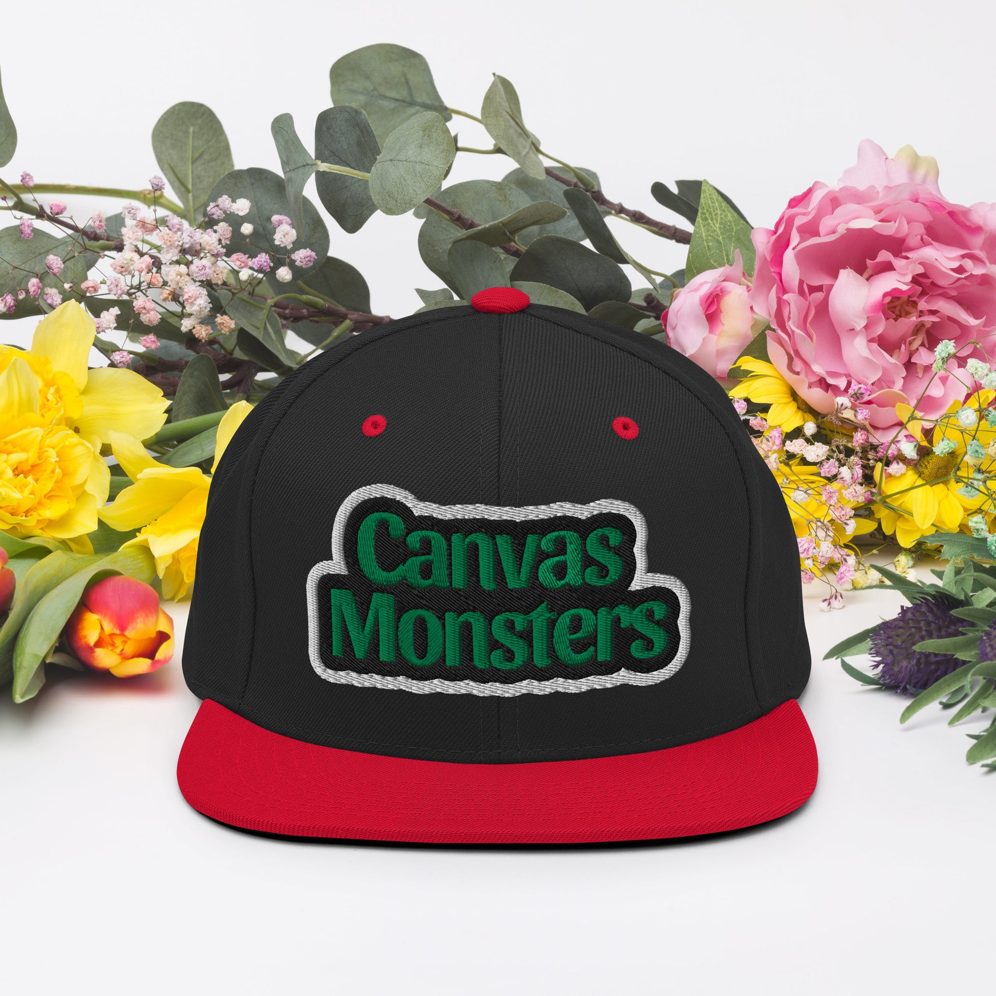 Black and red cap with 'Canvas Monsters' logo surrounded by flowers on a white background