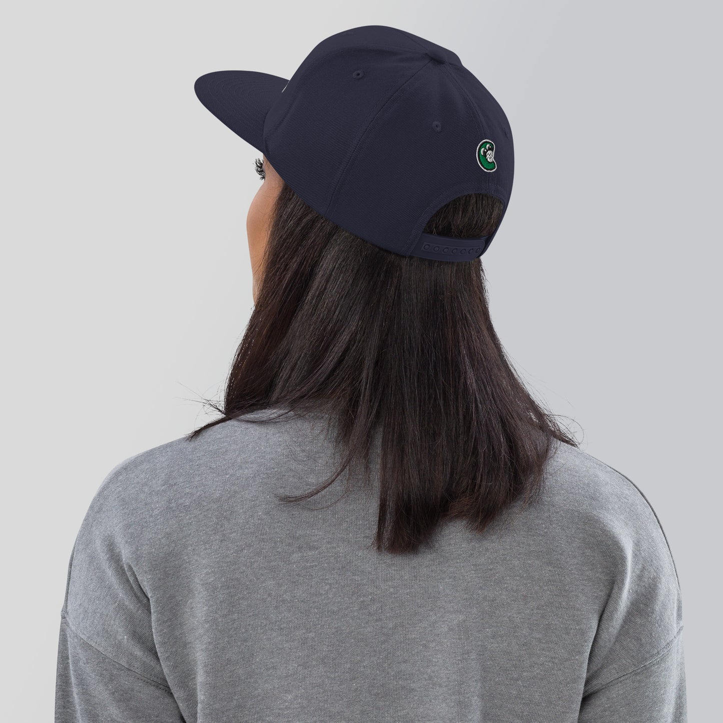 Person wearing a navy blue cap with a logo on the back, against a plain background