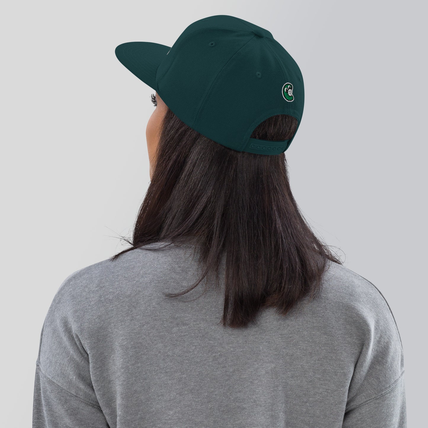 Person wearing a green cap with a logo on the back against a plain background