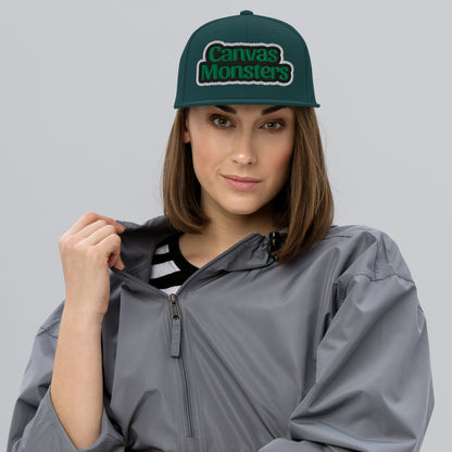 Woman wearing a gray raincoat and green 'Canvas Monsters' cap on a gray background