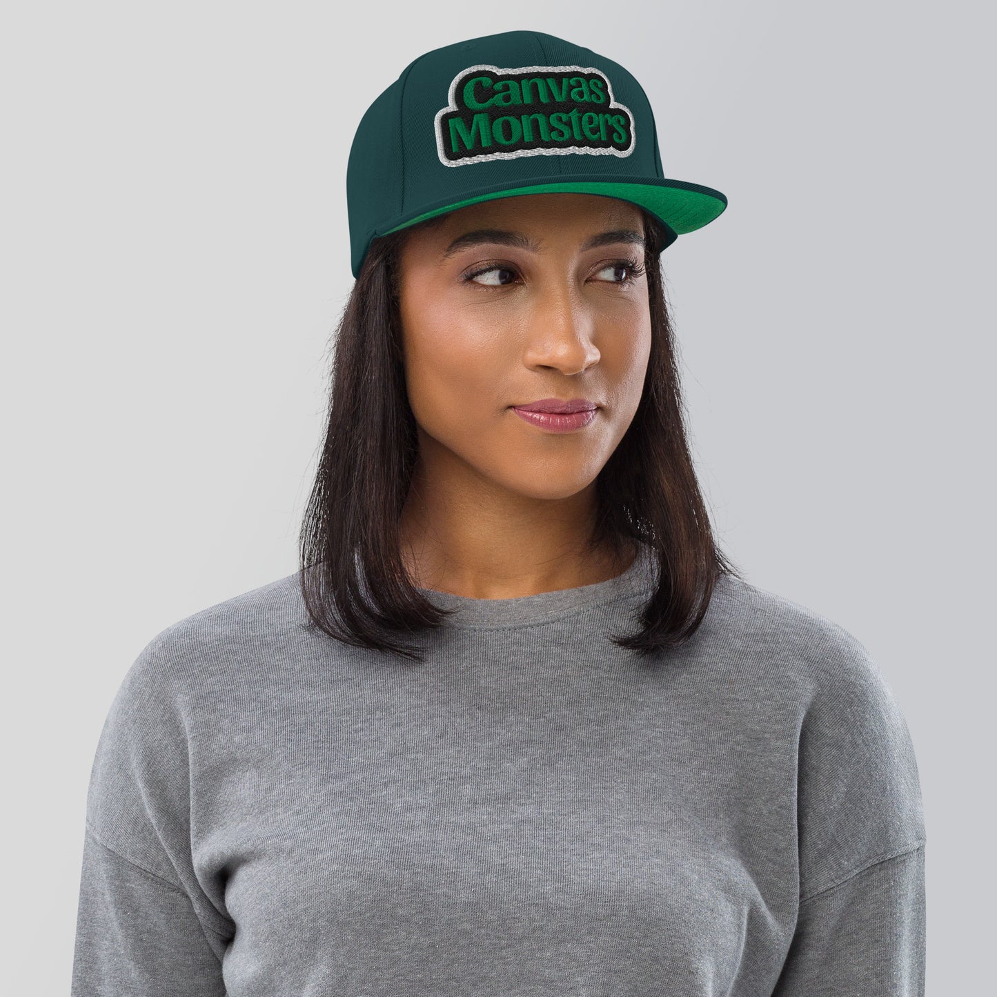 Person wearing a green 'Canvas Monsters' cap against a gray background
