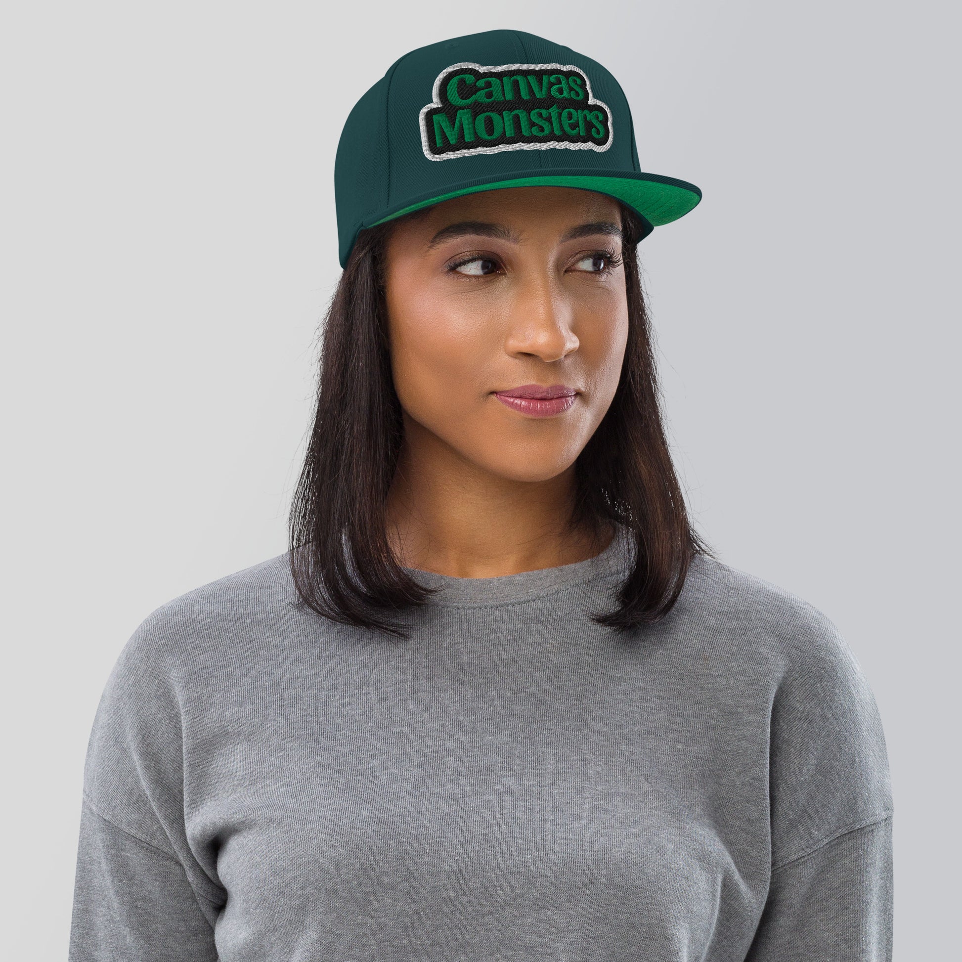 Person wearing a green 'Canvas Monsters' cap against a gray background