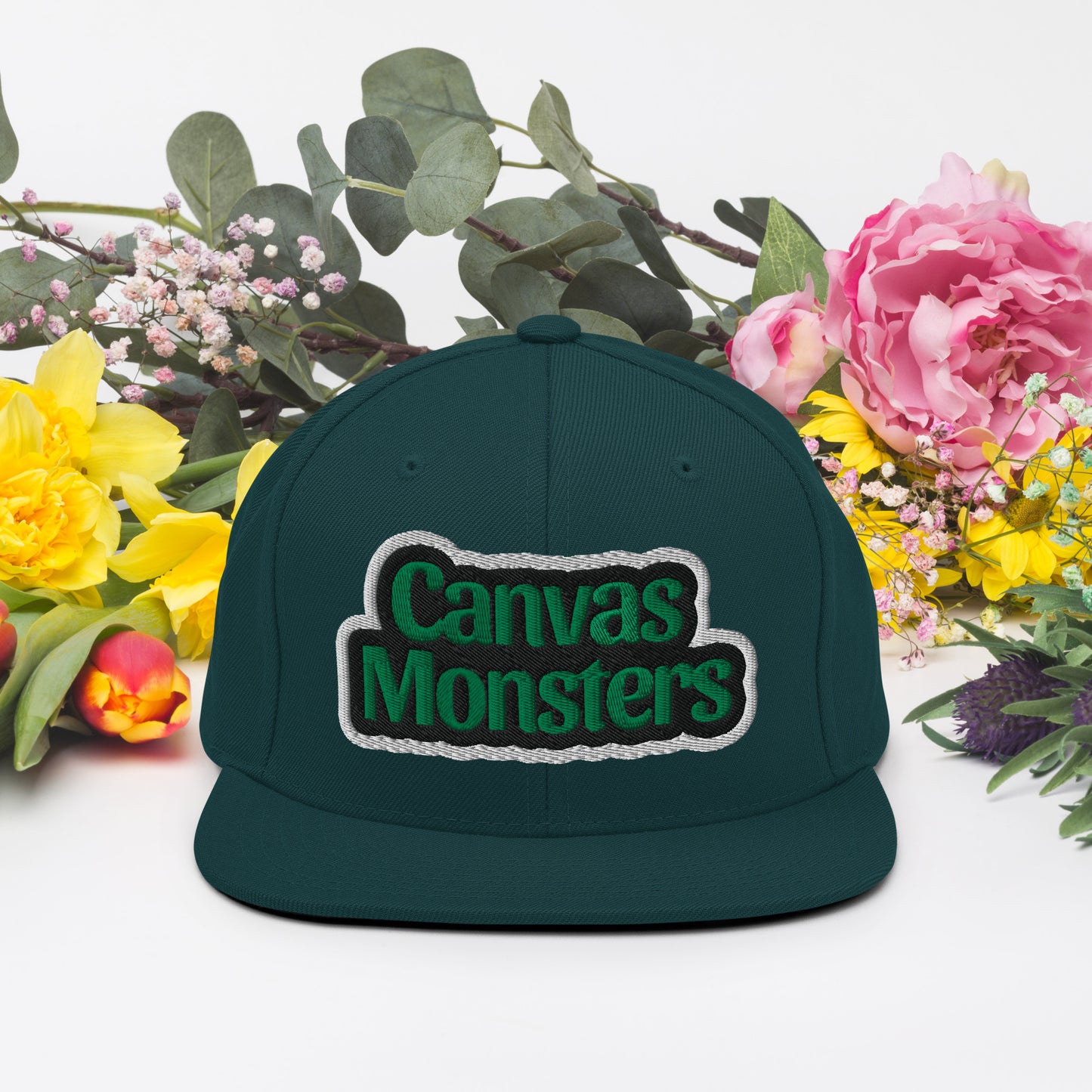 Green cap with 'Canvas Monsters' logo surrounded by flowers on a white background