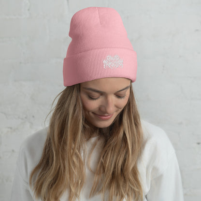Woman with long blonde hair wearing a light pink knit beanie with a metal text logo on the front.