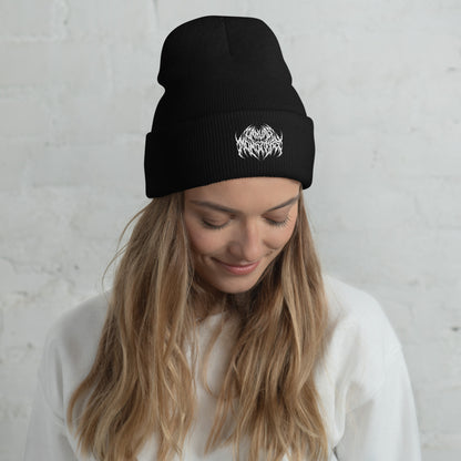 Woman with long blonde hair wearing a black knit beanie with a metal text logo on the front.