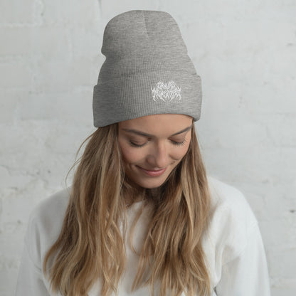 Woman with long blonde hair wearing a gray knit beanie with a metal text logo on the front.