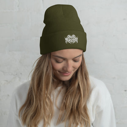 Woman with long blonde hair wearing an olive green knit beanie with a metal text logo on the front.