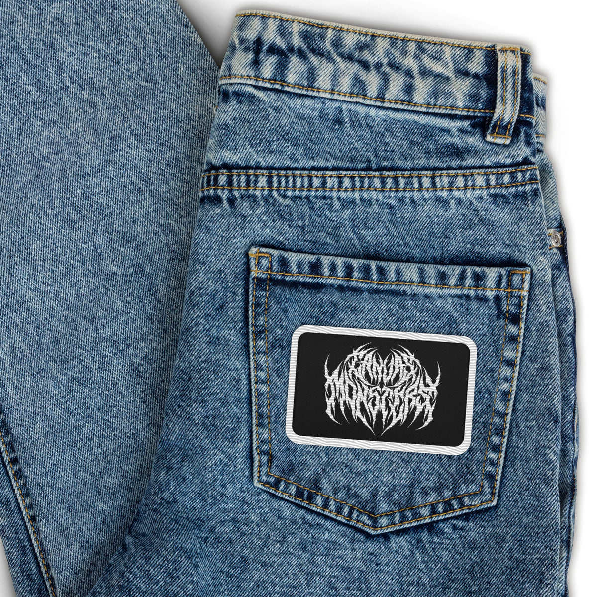 Embroidered patch with a white outline, black background and white embroidered design in metal lettering that reads "Canvas Monsters" on the back pocket of a pair of jeans.