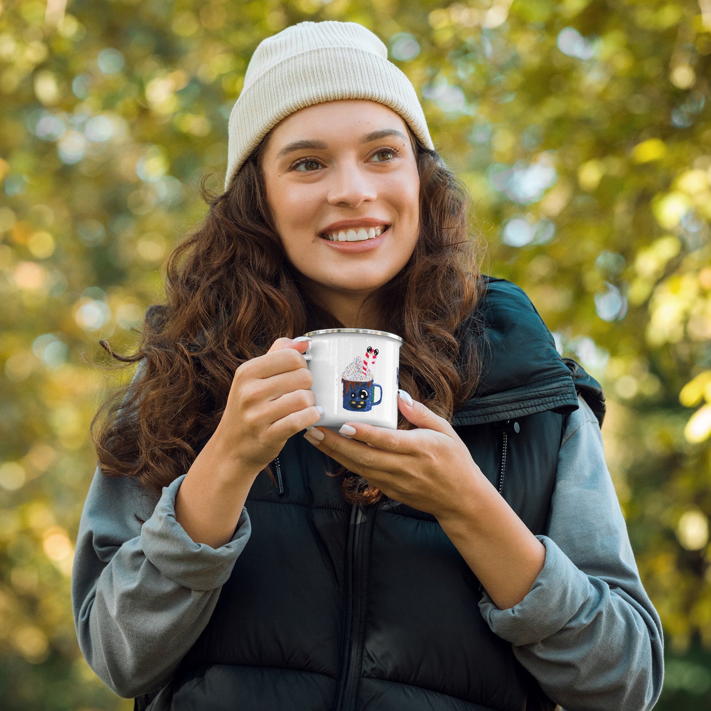 Woman standing outdoors, holding a camper mug featuring H. Coco