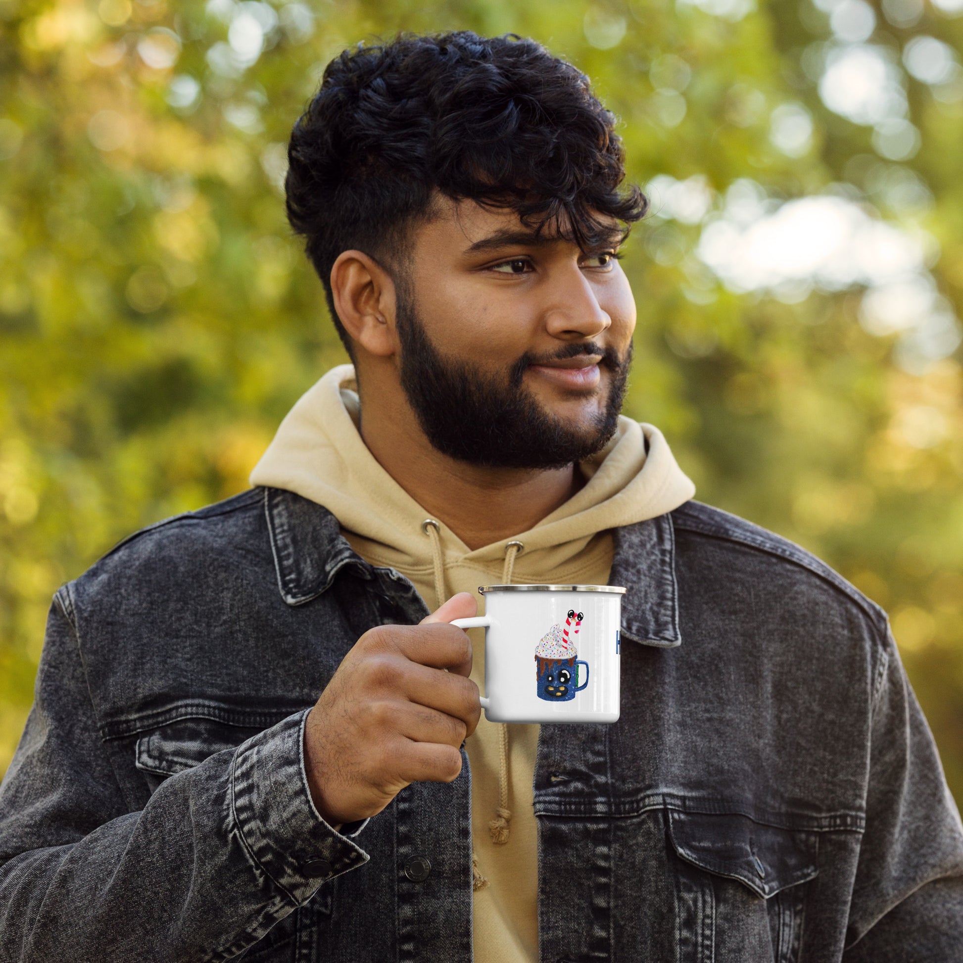 Man holding a camper mug featuring H. Coco outdoors with a blurred green background
