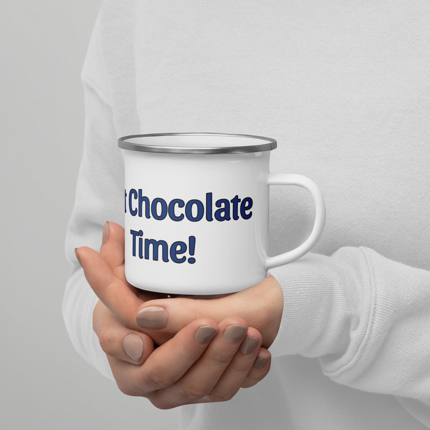 Person holding a white mug with 'Hot Chocolate Time!' text on a gray background
