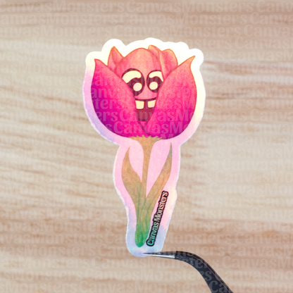 Holofoil sticker of a pink flower with a face on a wooden surface