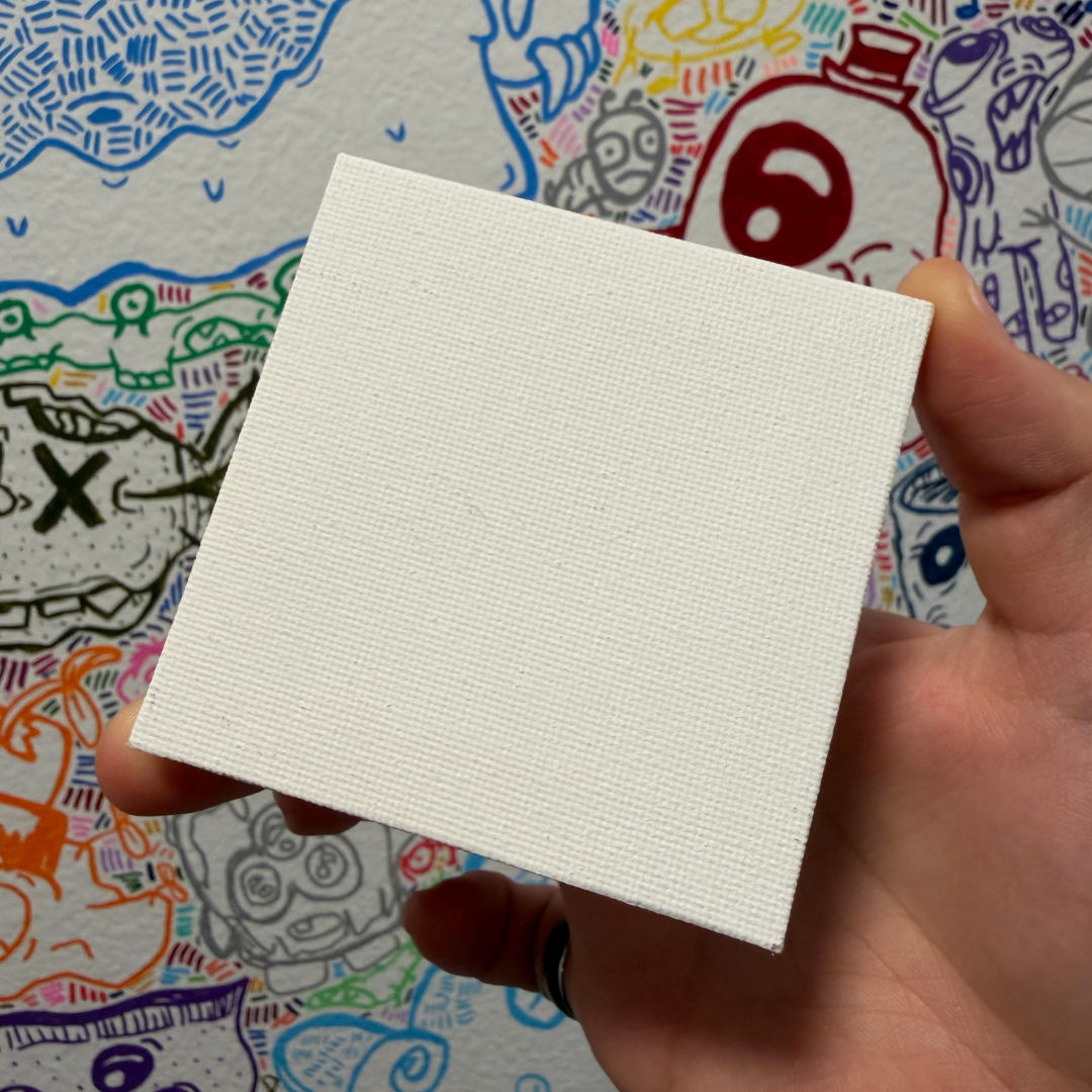 A hand holding a blank white textured square canvas or paint block in front of a colorful patterned background.