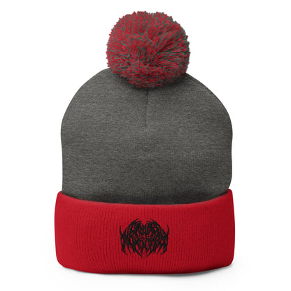Image of a knit beanie with a pom pom on top, in red and gray with a metal text logo on the front.