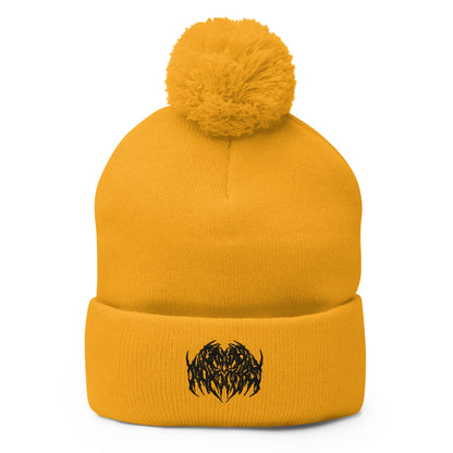 Image of a knit beanie with a pom pom on top, in golden yellow with a metal text logo on the front.