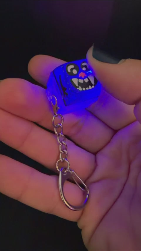 Video of a key cap keychain against a black background. Cap is painted with a blue monster character.
