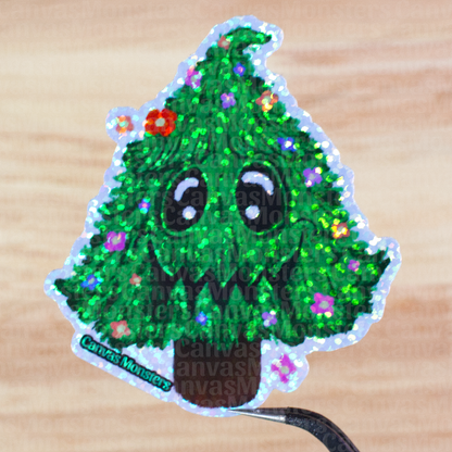 Glitter sticker of a green tree with facial features and flowers held above a wooden surface