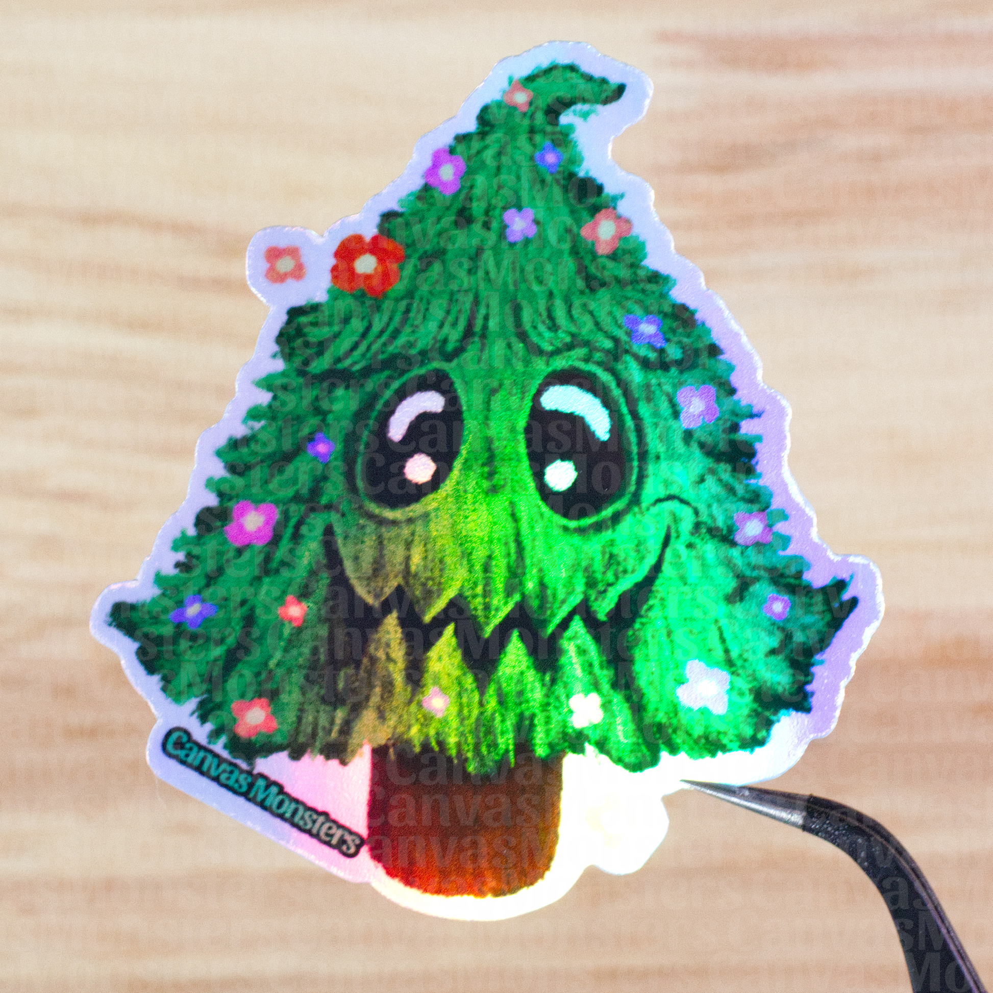 Holofoil sticker of a green tree with facial features and flowers held above a wooden surface