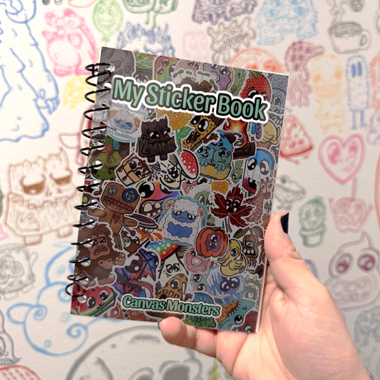 A book that reads My Sticker Book in green text. Surrounded by small cartoon monsters on the book cover. The book has a black spiral binding. Being held up in hand, in front of a white wall with many small monster doodles. 