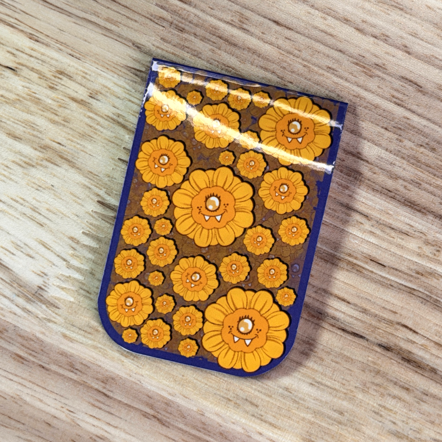 Magnetic Bookmark with a blue border and a pattern of cartoon sunflowers, sitting on a wooden surface