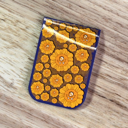 Magnetic Bookmark with a blue border and a pattern of cartoon sunflowers, sitting on a wooden surface