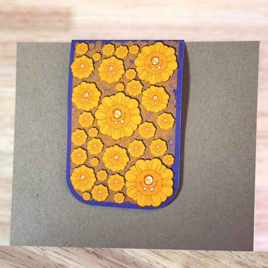 Magnetic Bookmark with a blue border and a pattern of cartoon sunflowers, folded over a piece of paper.