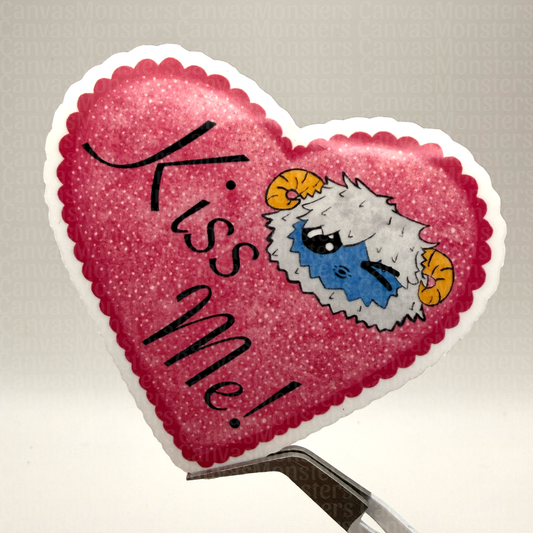 Heart-shaped pink sticker with 'Kiss Me!' text and cartoon yeti character held in front of a white background